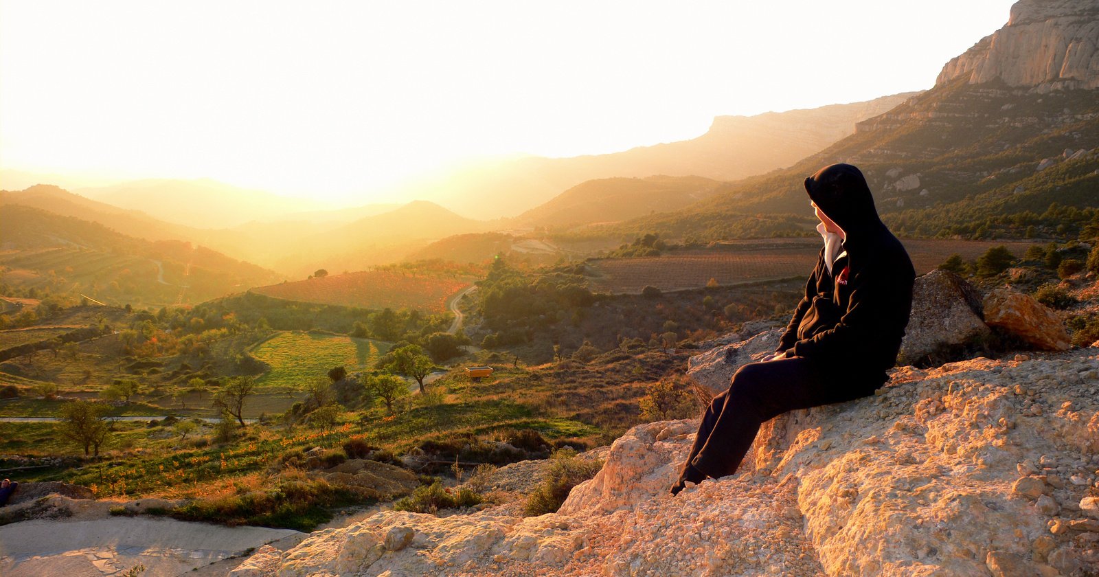 A photo of a woman sat overlooking a beautiful view in South African vineyards and mountains as the sun sets